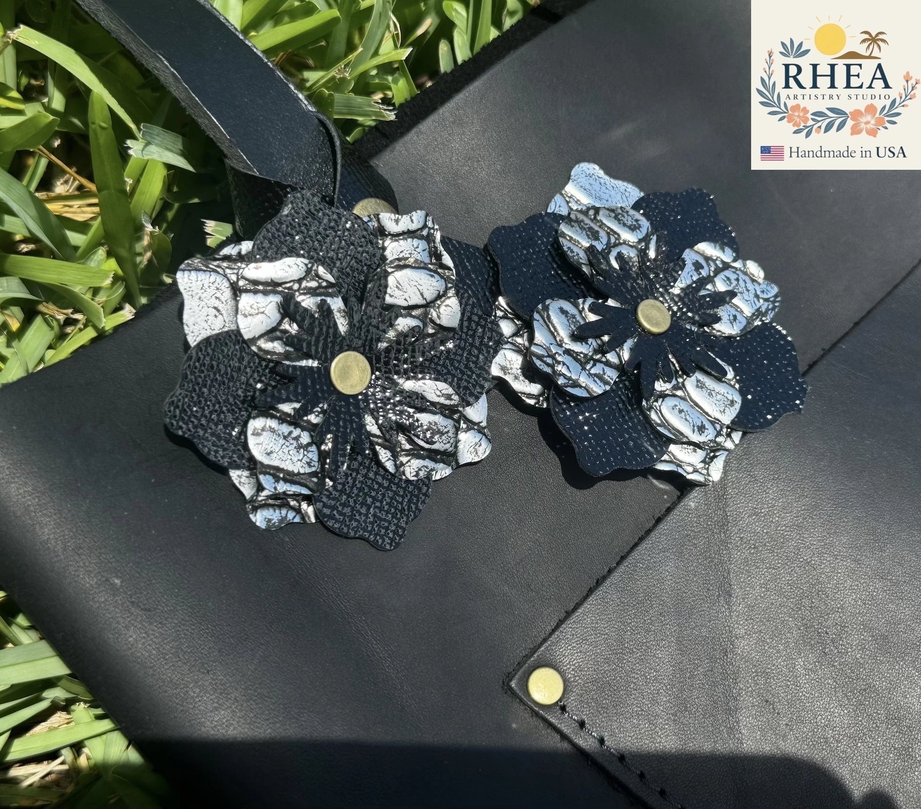 Rhea Artistry Studio double leather flower charm in silver and black with brass rivets, attached to a black leather accessory.