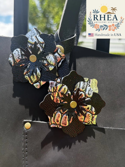 Rhea Artistry Studio handcrafted double leather flower charm in silver and black with brass rivets, attached to a black leather bag.