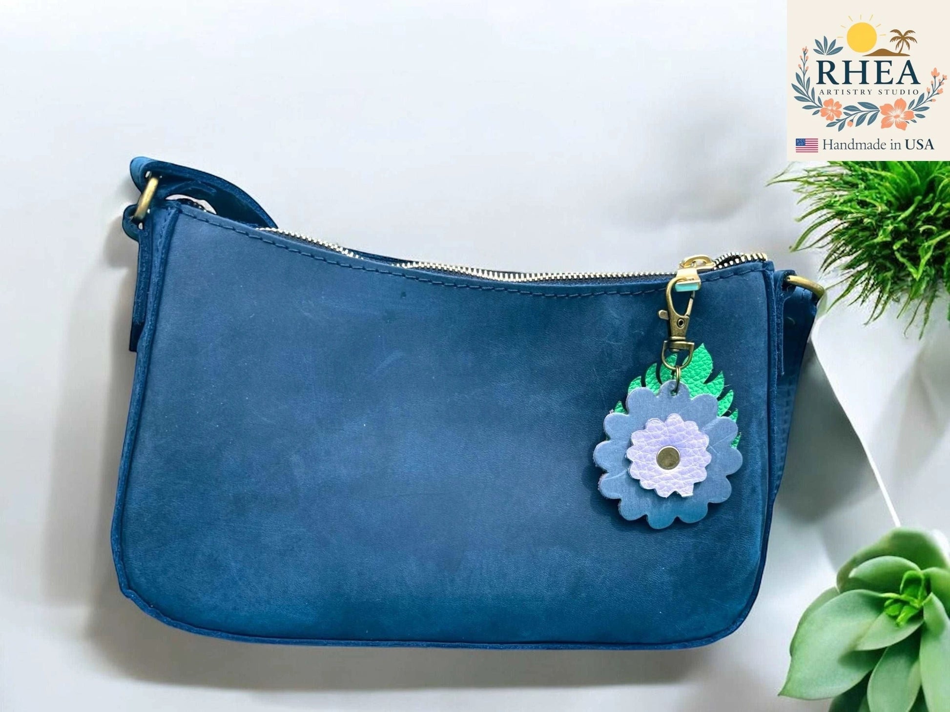 Rhea Artistry Studio blue leather monstera leaf and flower charm with brass clasp on navy blue purse.