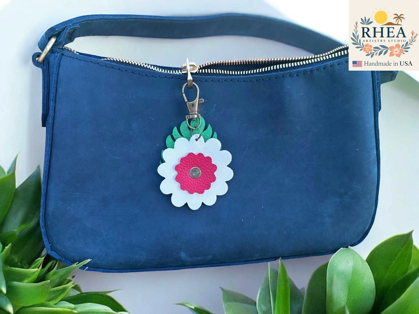 Rhea Artistry Studio leather monstera leaf and flower charm with white petals, pink center, and green leaves, attached to a navy blue purse zipper.