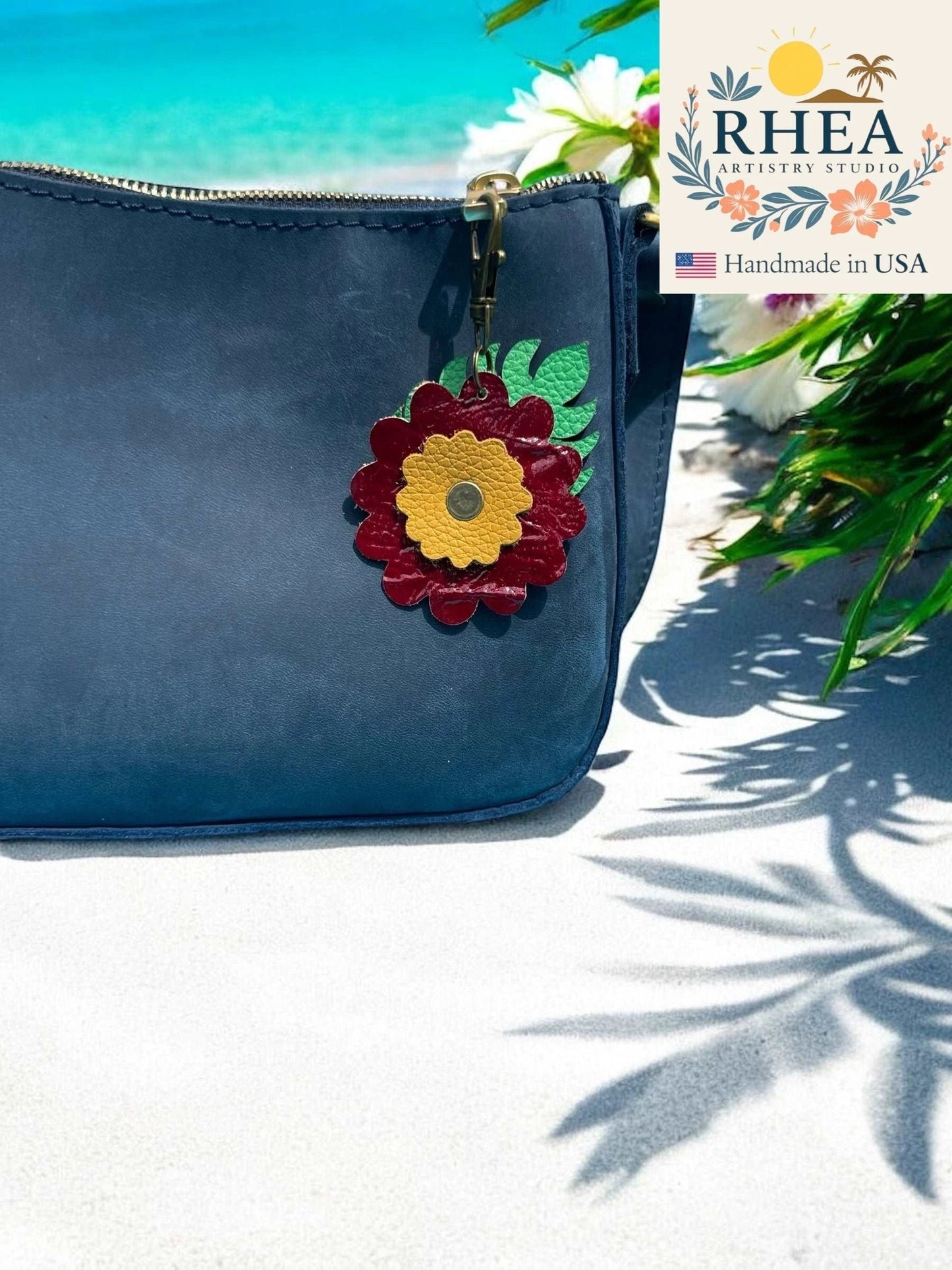 Rhea Artistry Studio leather monstera leaf and flower charm with brass lobster clasp on a navy purse.