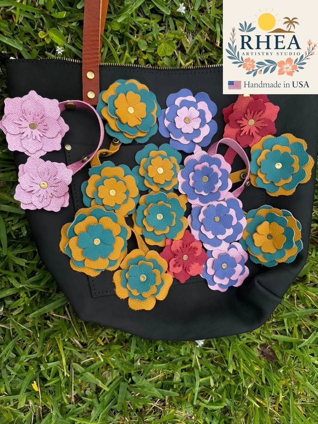Rhea Artistry Studio handmade leather flower charms in blue bell, barbie pink, teal, mustard, and red. Layered leather blooms with brass rivets.