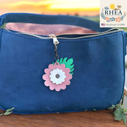 Rhea Artistry Studio leather monstera leaf and flower charm with pink and white petals on a navy blue purse zipper.