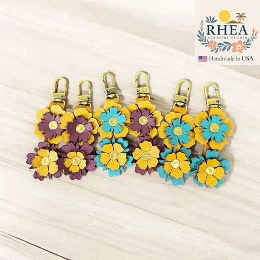 Rhea Artistry Studio handmade leather zipper pulls with stacked floral designs in yellow, purple, and teal with brushed brass clasps.