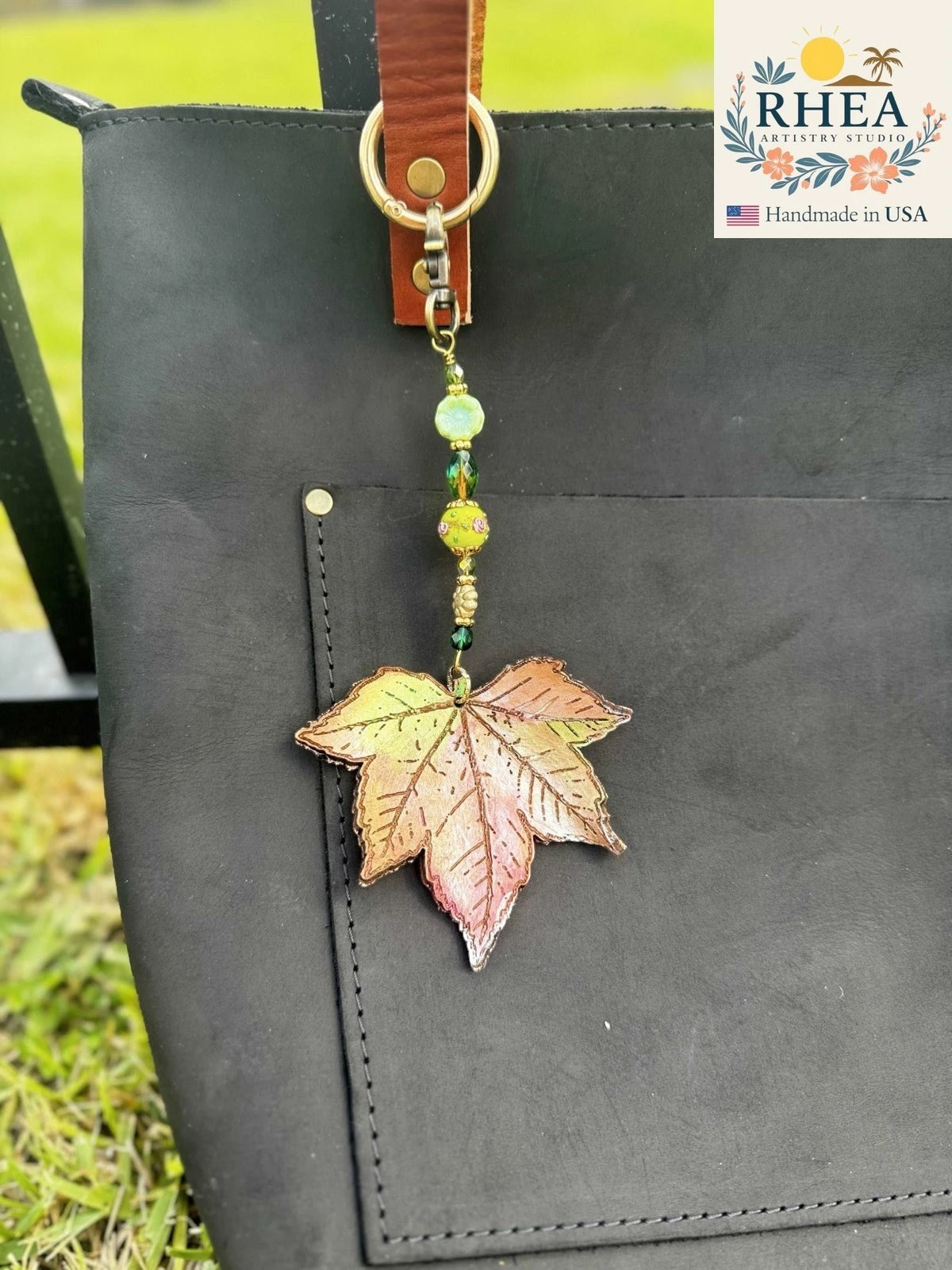 Rhea Artistry Studio Garden Lagoon Bloom leather charm with maple leaf design, Czech glass beads, and brass hardware on a black tote bag.