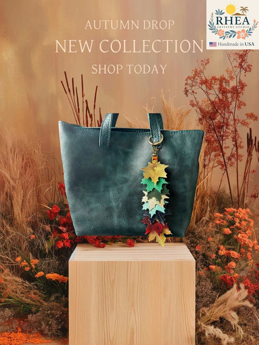 Rhea Artistry Studio handcrafted leather maple leaf bag charm in multi-color, attached to a teal tote bag.