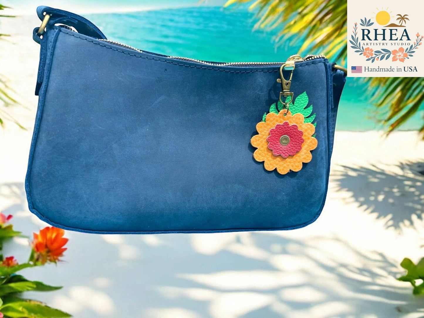 Rhea Artistry Studio blue leather purse with a yellow and pink leather monstera leaf flower charm attached to the zipper.