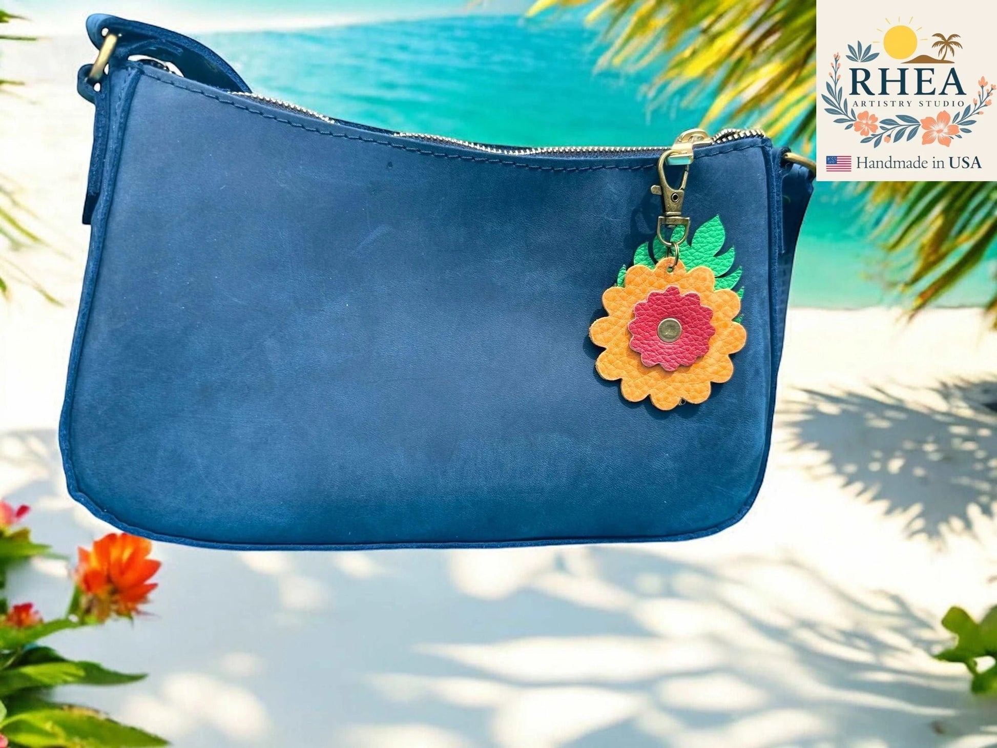 Rhea Artistry Studio blue leather purse with a yellow and pink leather monstera leaf flower charm attached to the zipper.