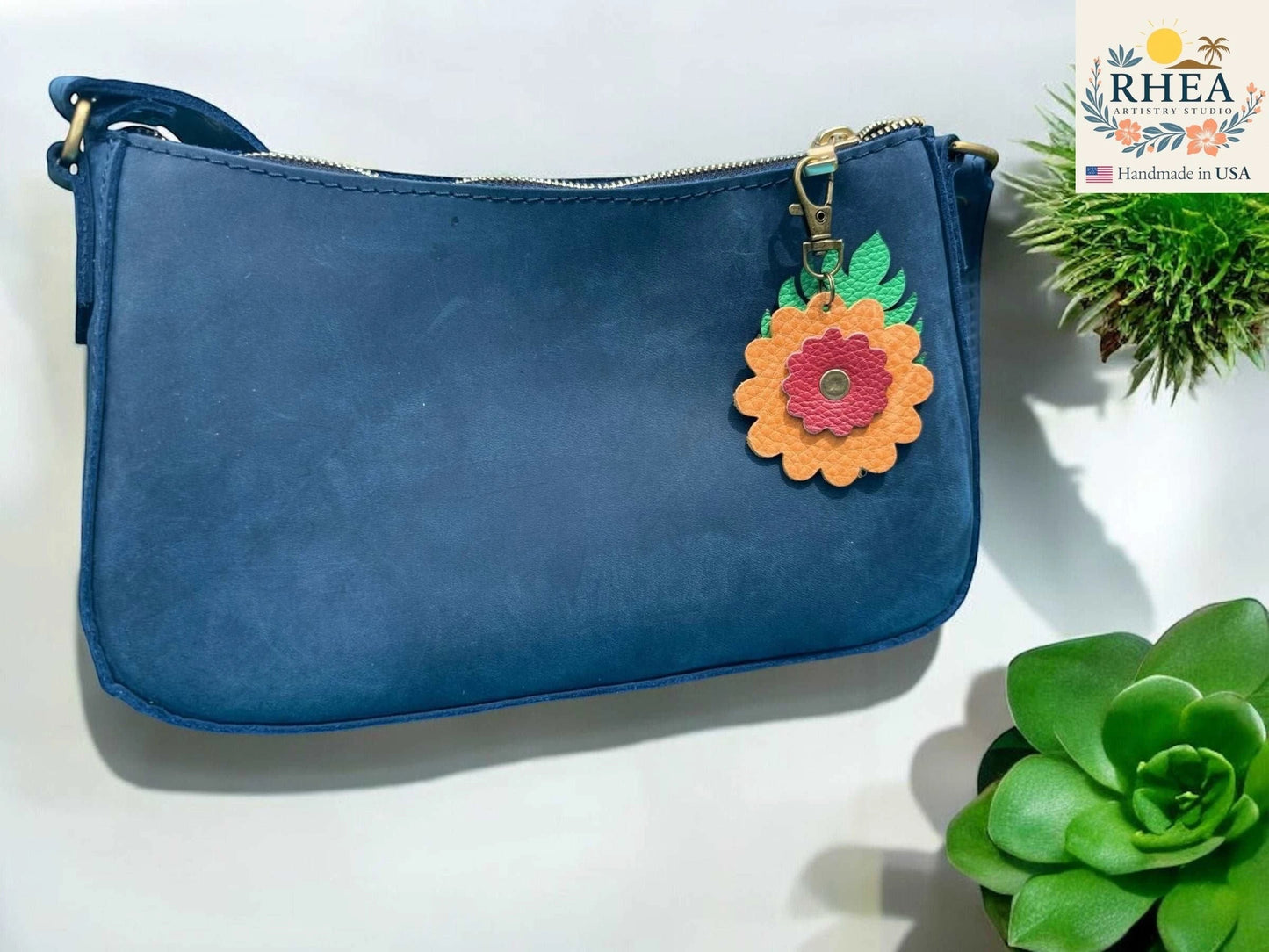 Rhea Artistry Studio blue leather monstera leaf and flower charm with brass clasp on a navy blue purse.