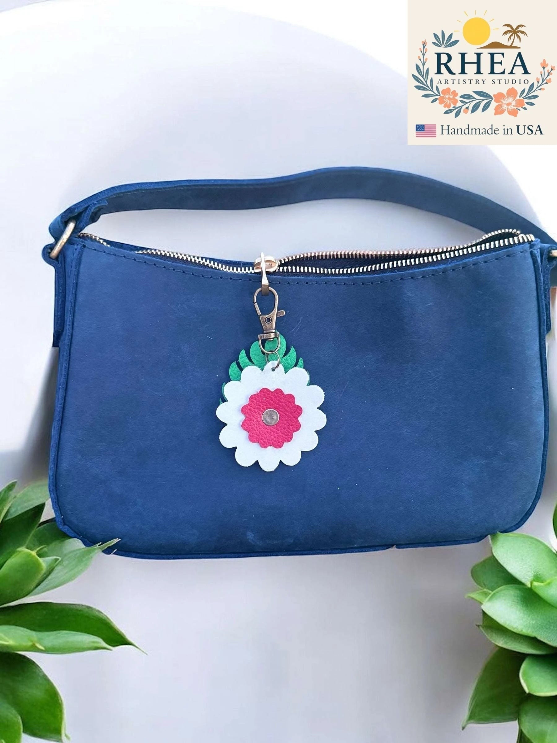 Rhea Artistry Studio leather monstera leaf and flower charm with white and pink petals, attached to a navy blue purse zipper.