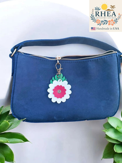 Rhea Artistry Studio leather monstera leaf and flower charm with white and pink petals, attached to a navy blue purse zipper.