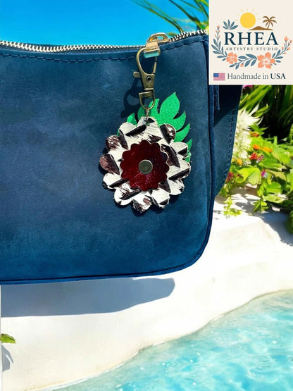 Rhea Artistry Studio leather monstera leaf and flower charm with brass lobster clasp on a navy blue purse.
