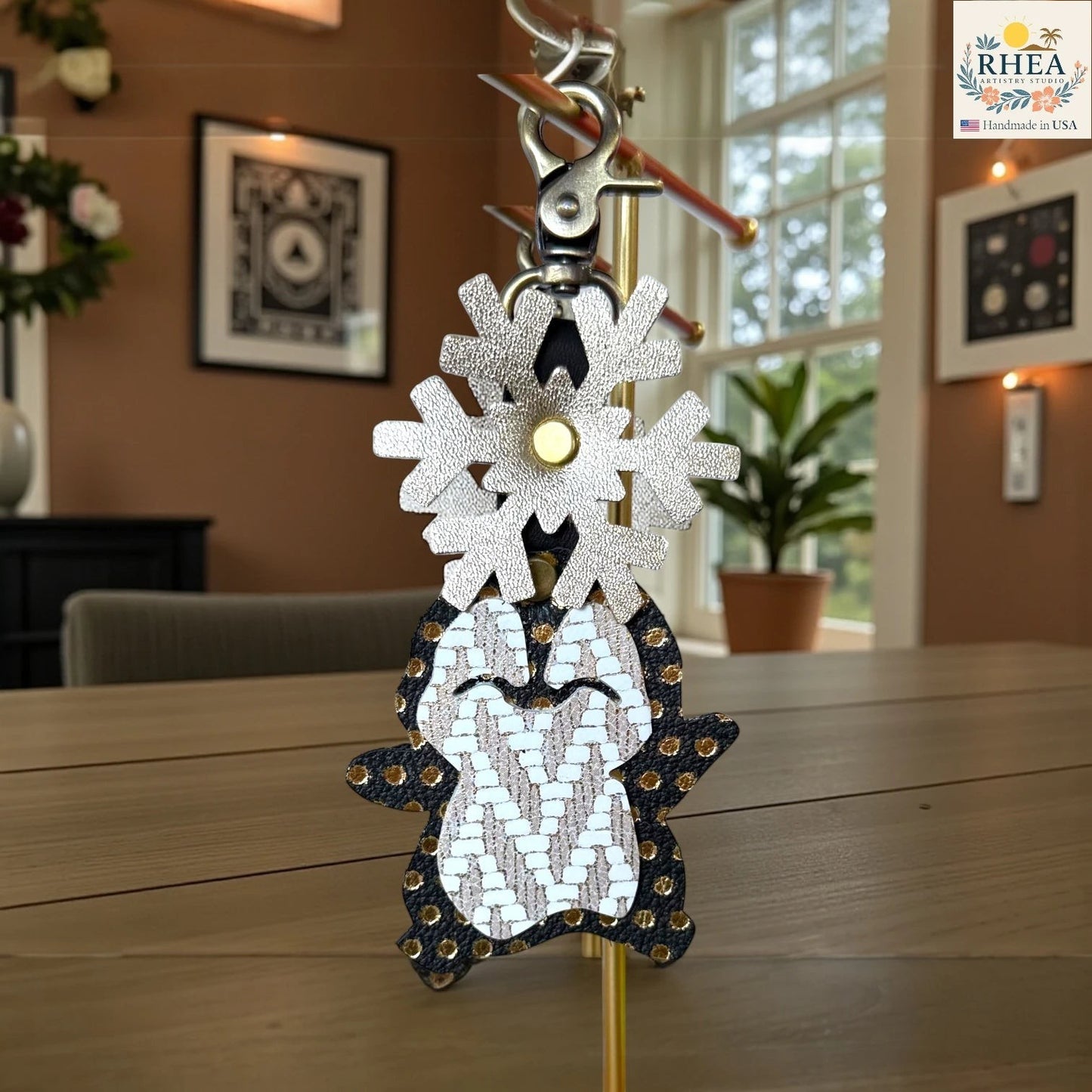 Rhea Artistry Studio handmade leather penguin charm with snowflake detail, black with gold studs and white/tan patterned body.