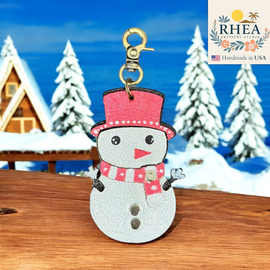 Rhea Artistry Studio handmade leather snowman charm with red hat and scarf, silver body, and festive details. Lobster clasp for bag or purse.