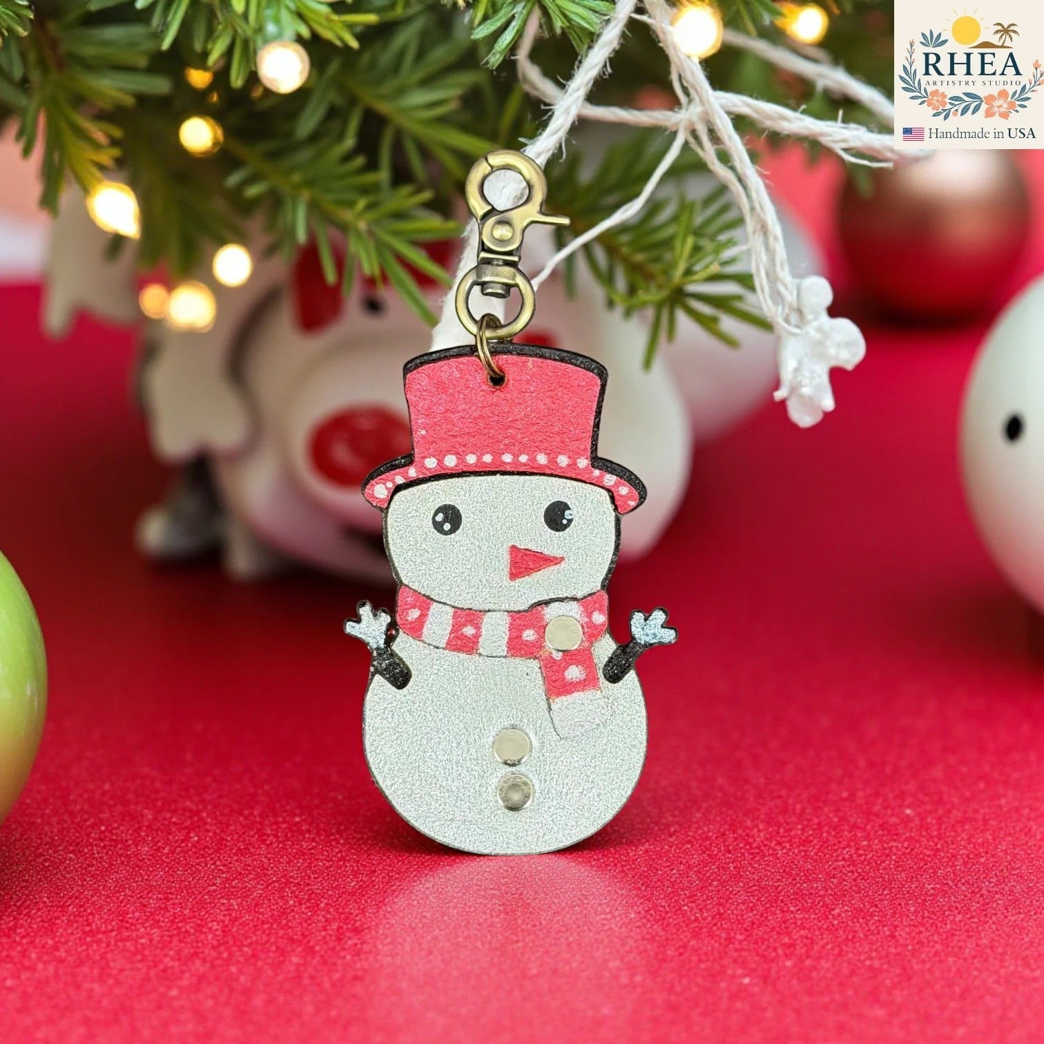 Rhea Artistry Studio handmade leather snowman charm with red hat and scarf, silver body, and rivet buttons. Festive winter accessory.