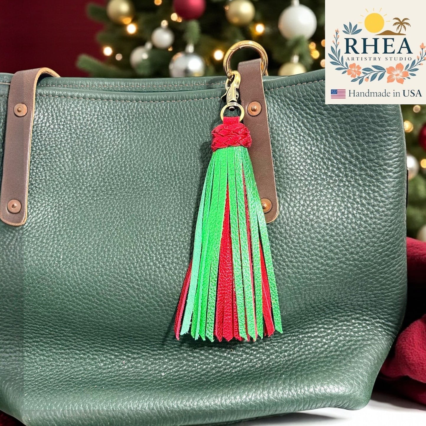 Rhea Artistry Studio handmade leather tassel bag charm in red and green with antique brass clasp, attached to a green pebbled leather tote bag.