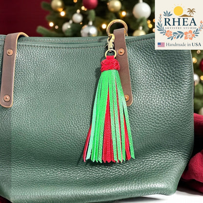 Rhea Artistry Studio handmade leather tassel bag charm in red and green with antique brass clasp, attached to a green pebbled leather tote bag.