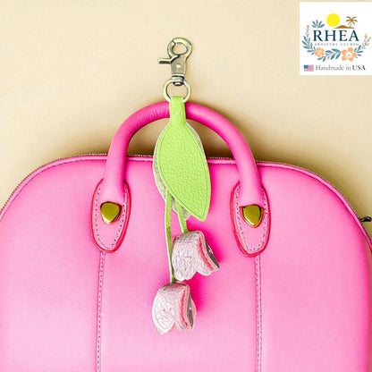 Rhea Artistry Studio handmade leather tulip charm with green leaf and silver-pink flowers, attached to a pink handbag.