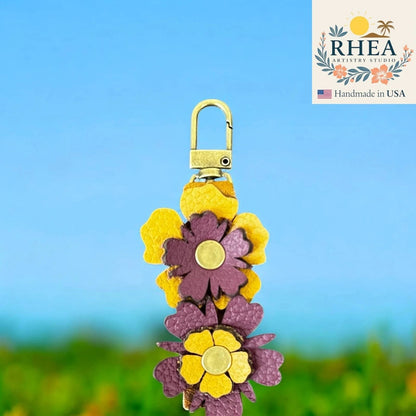 Rhea Artistry Studio handmade leather zipper pull with stacked purple and yellow wildflowers and brushed brass clasp.