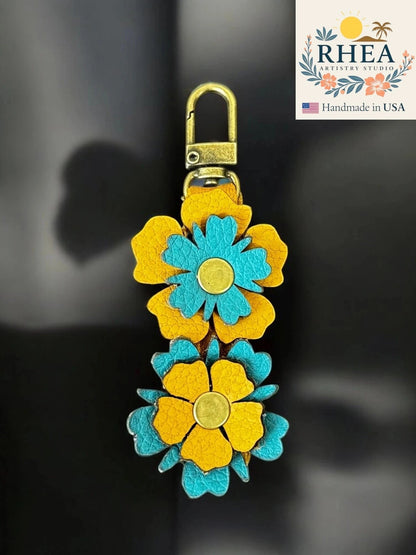Rhea Artistry Studio handmade leather zipper pull with two stacked yellow and teal wildflowers and brushed brass clasp.