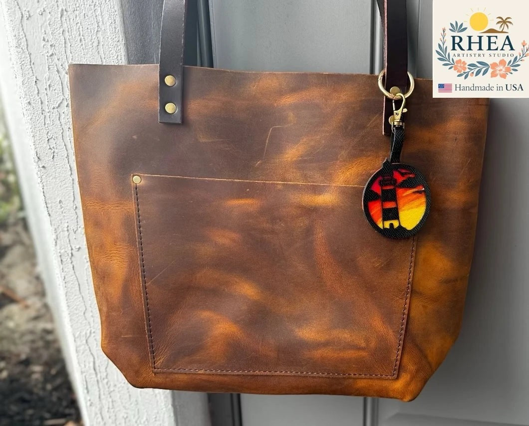 Rhea Artistry Studio hand-painted leather lighthouse bag charm with coastal sunset scene on vegetable-tanned leather.