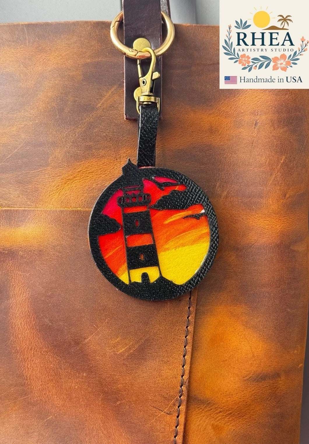 Rhea Artistry Studio hand-painted leather lighthouse charm with coastal sunset scene on vegetable-tanned leather.