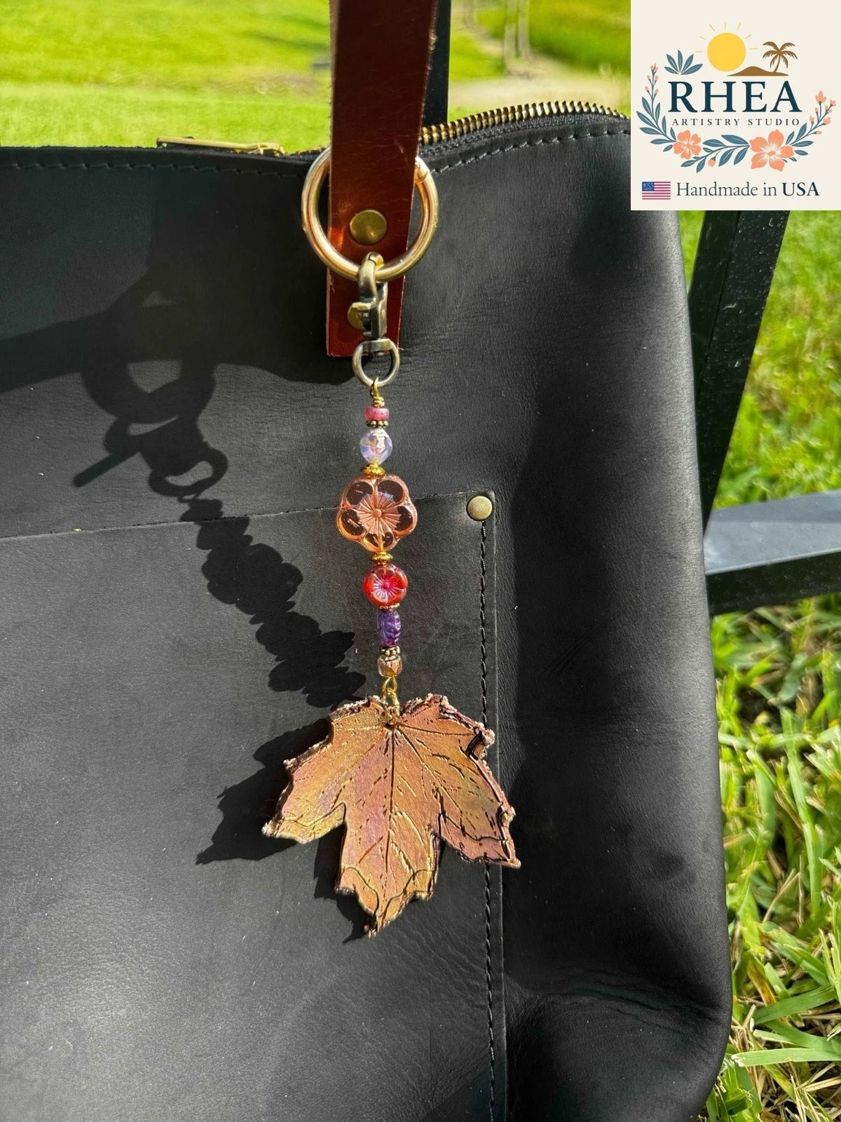 Rhea Artistry Studio handcrafted maple leaf charm with Czech glass beads on a black leather tote bag.