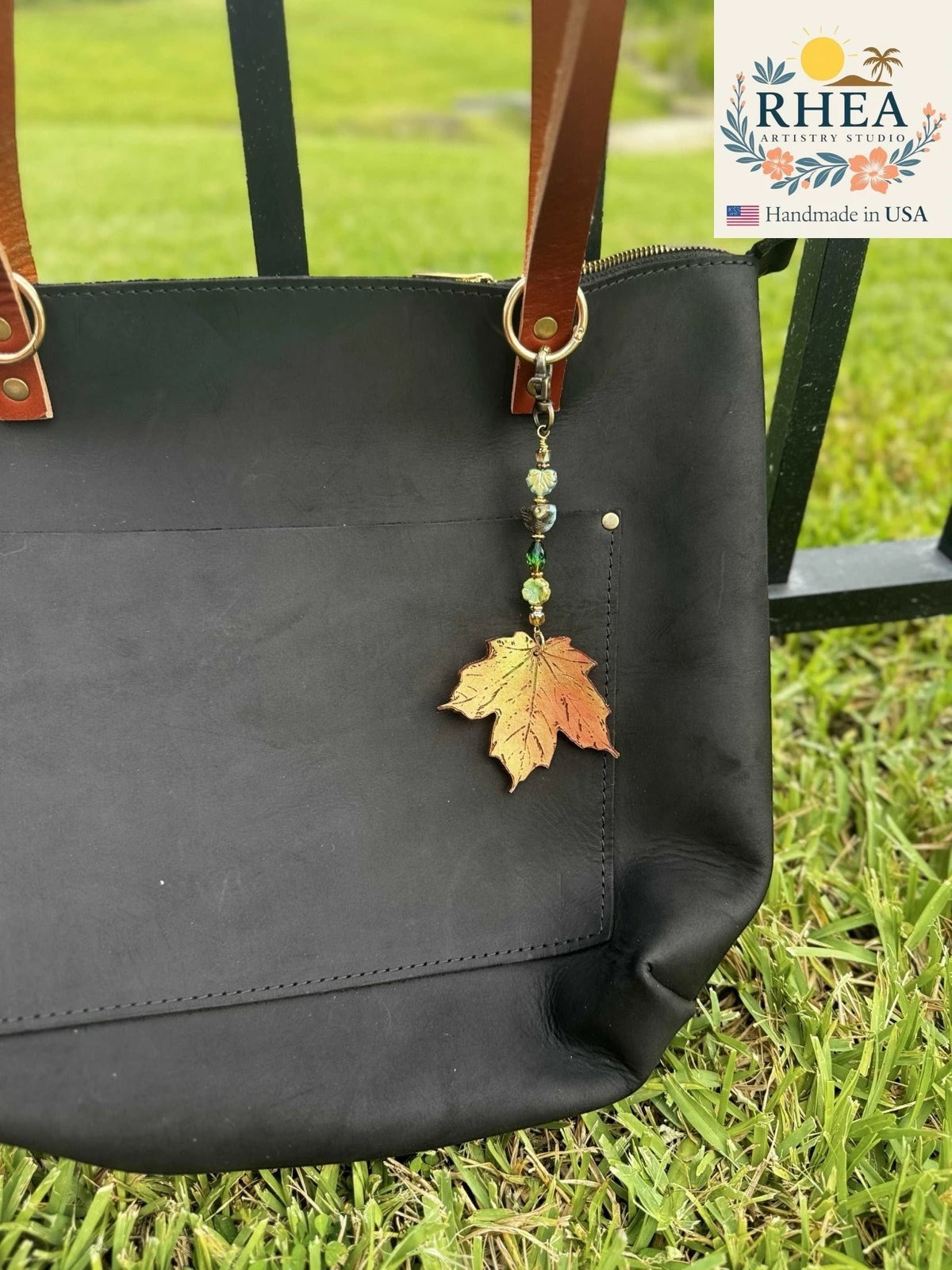 Rhea Artistry Studio handcrafted maple leaf charm with green beads on a black leather tote bag.