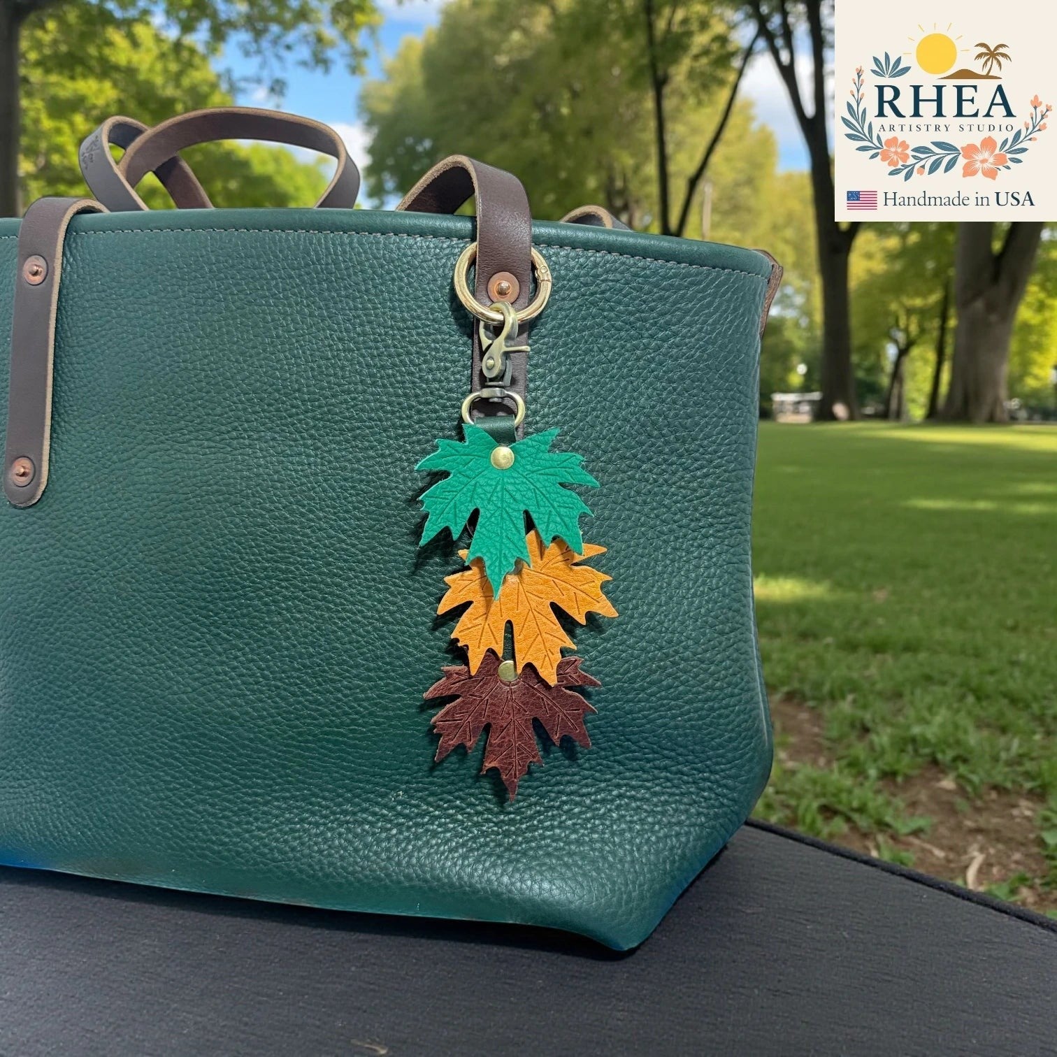 Rhea Artistry Studio layered maple leaf leather bag charm in green, orange, and brown with vein detail, attached to a dark green tote bag.