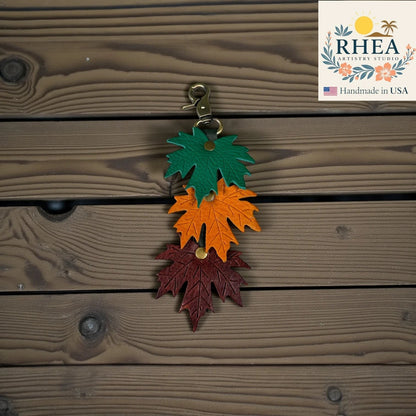 Rhea Artistry Studio layered maple leaf leather bag charm in green, orange, and burgundy with vein detail and brass hardware.
