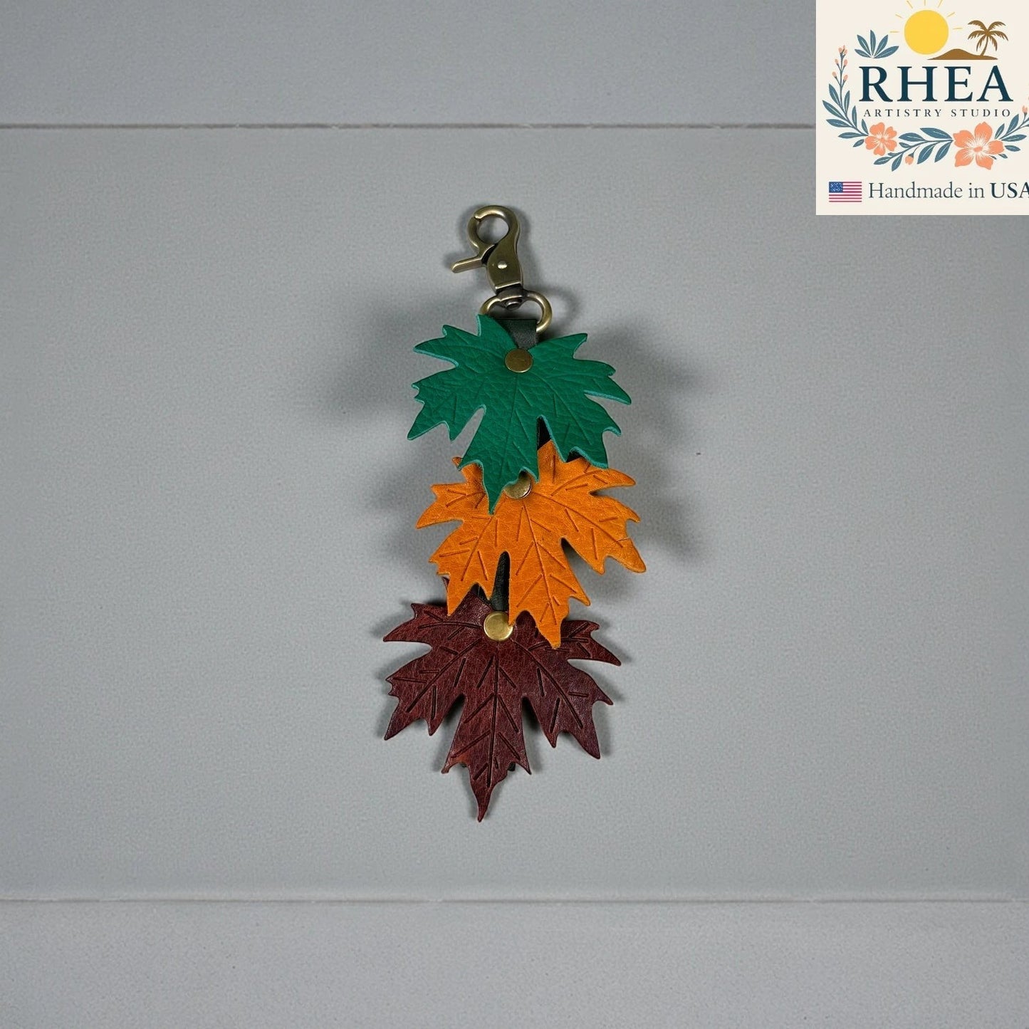 Rhea Artistry Studio layered maple leaf leather bag charm in green, orange, and burgundy with vein detail and brass hardware.