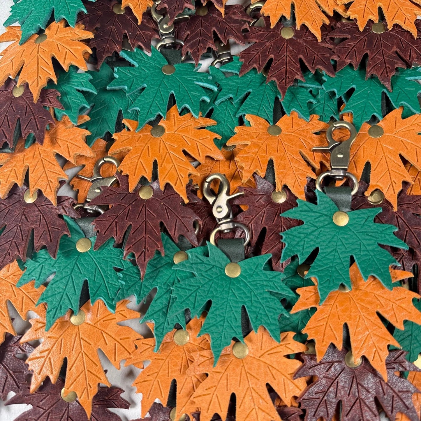 Rhea Artistry Studio layered maple leaf leather bag charm in green, orange, and brown with embossed vein detail and brass hardware.