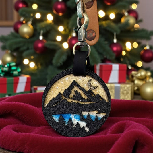 Rhea Artistry Studio hand-painted leather charm featuring a layered winter mountain and forest silhouette with a crescent moon and sunset sky.