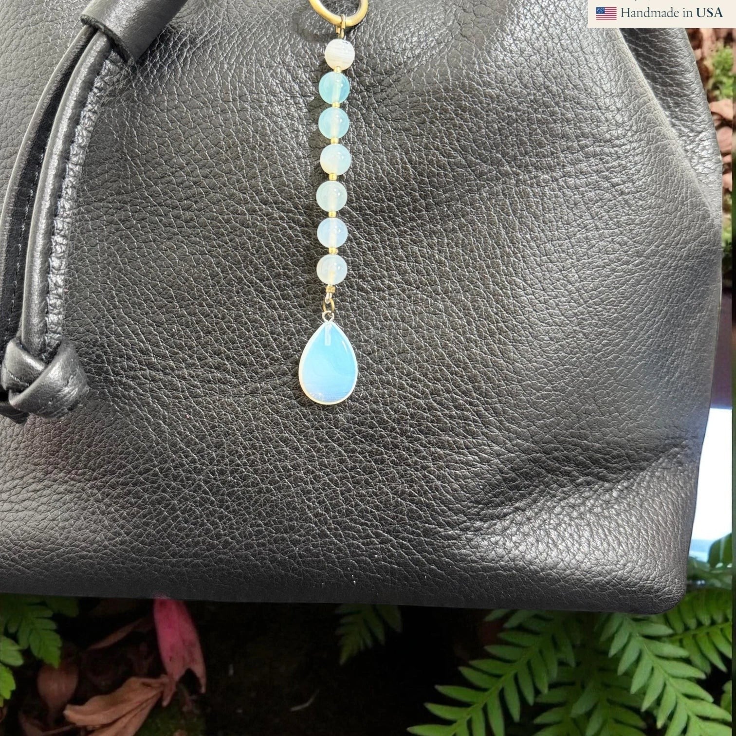 Rhea Artistry Studio Opalite Teardrop Charm with white and pale blue beads on a black leather bag.
