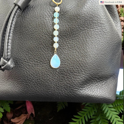 Rhea Artistry Studio Opalite Teardrop Charm with white and pale blue beads on a black leather bag.