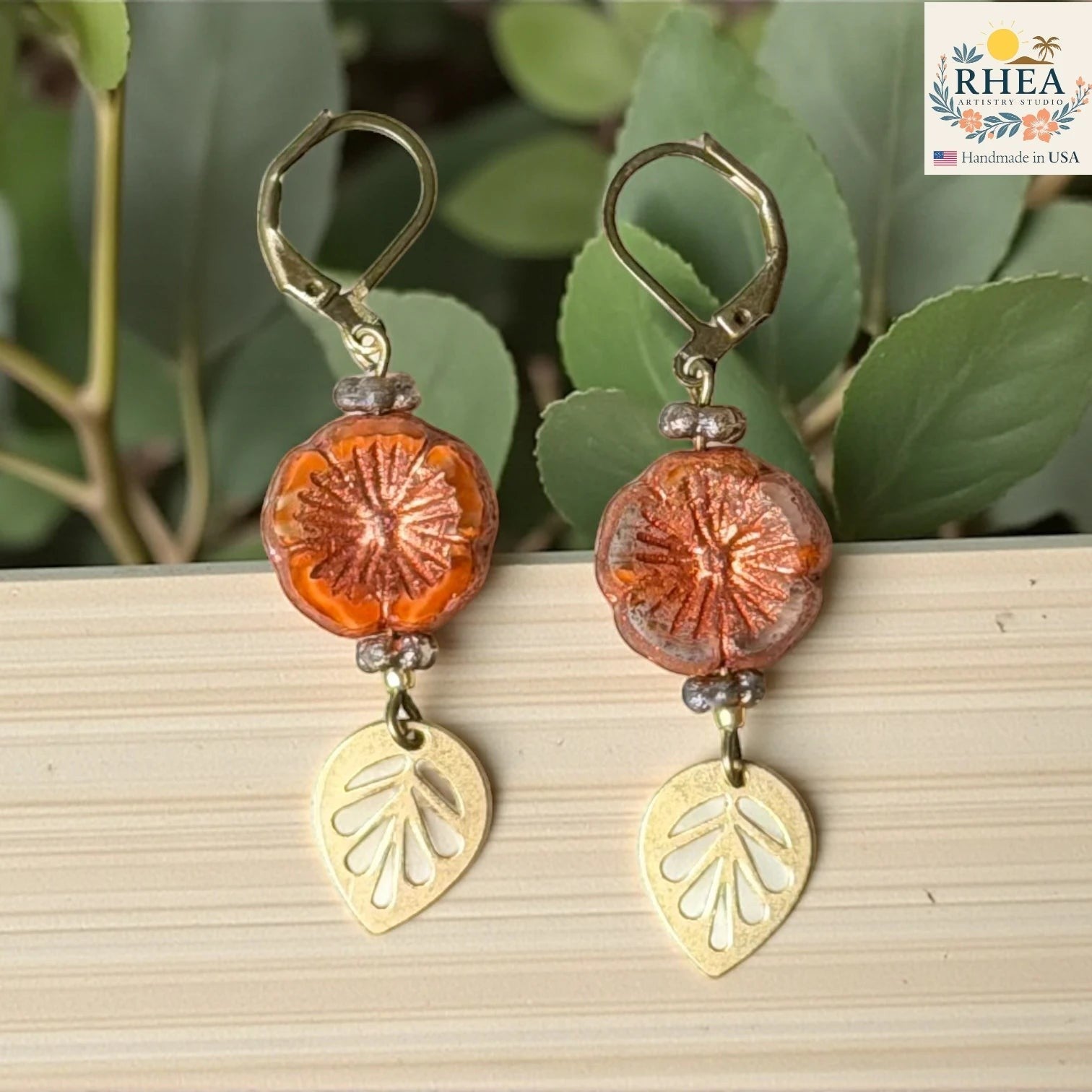 Rhea Artistry Studio orange hibiscus glass drop earrings with gold leaf charms and lever back hooks.