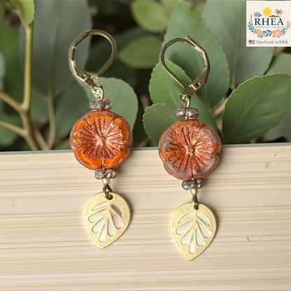 Rhea Artistry Studio orange hibiscus glass drop earrings with gold leaf charms and lever back hooks.