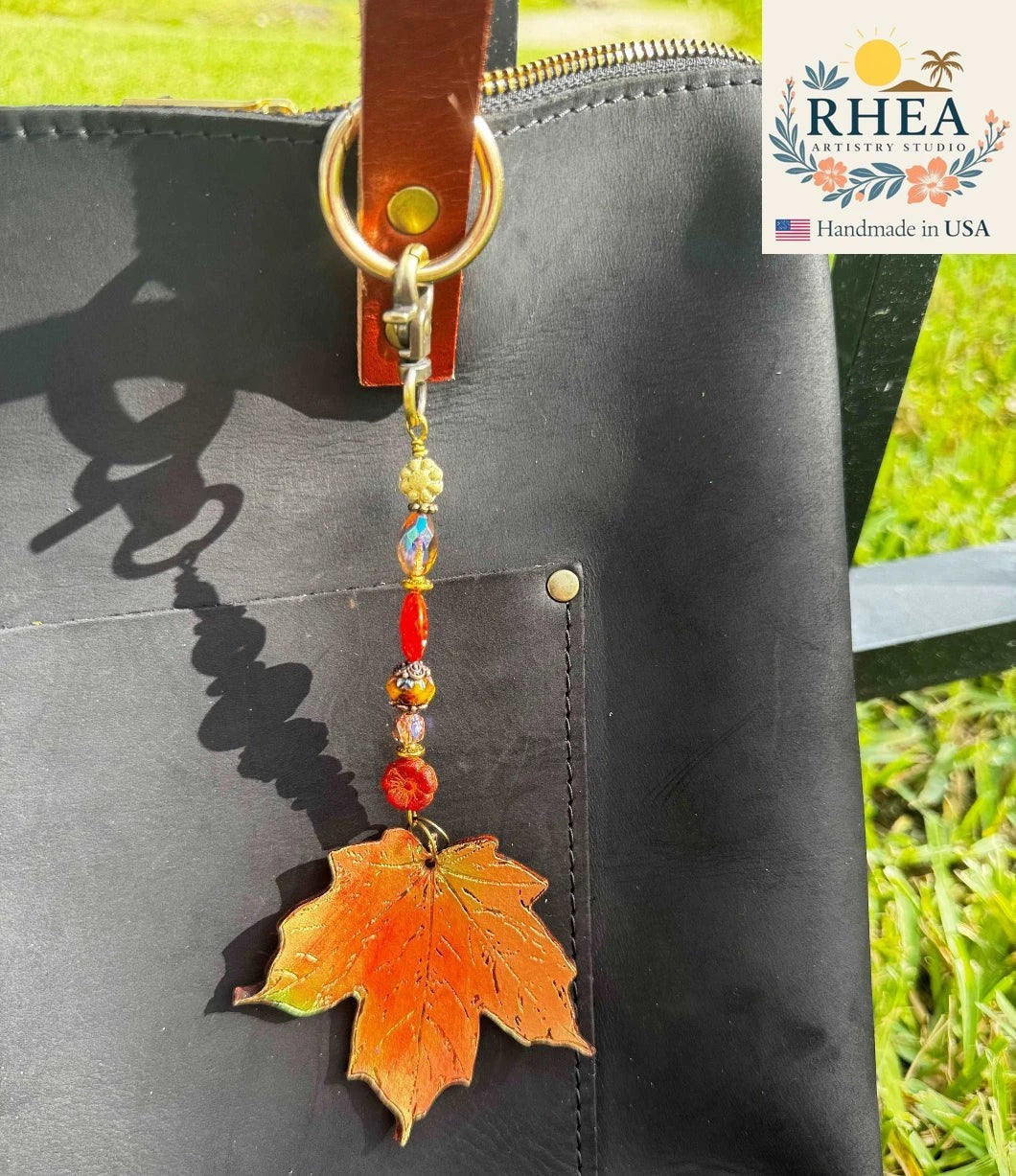 Rhea Artistry Studio orange maple leaf charm with colorful beads on a black leather bag.