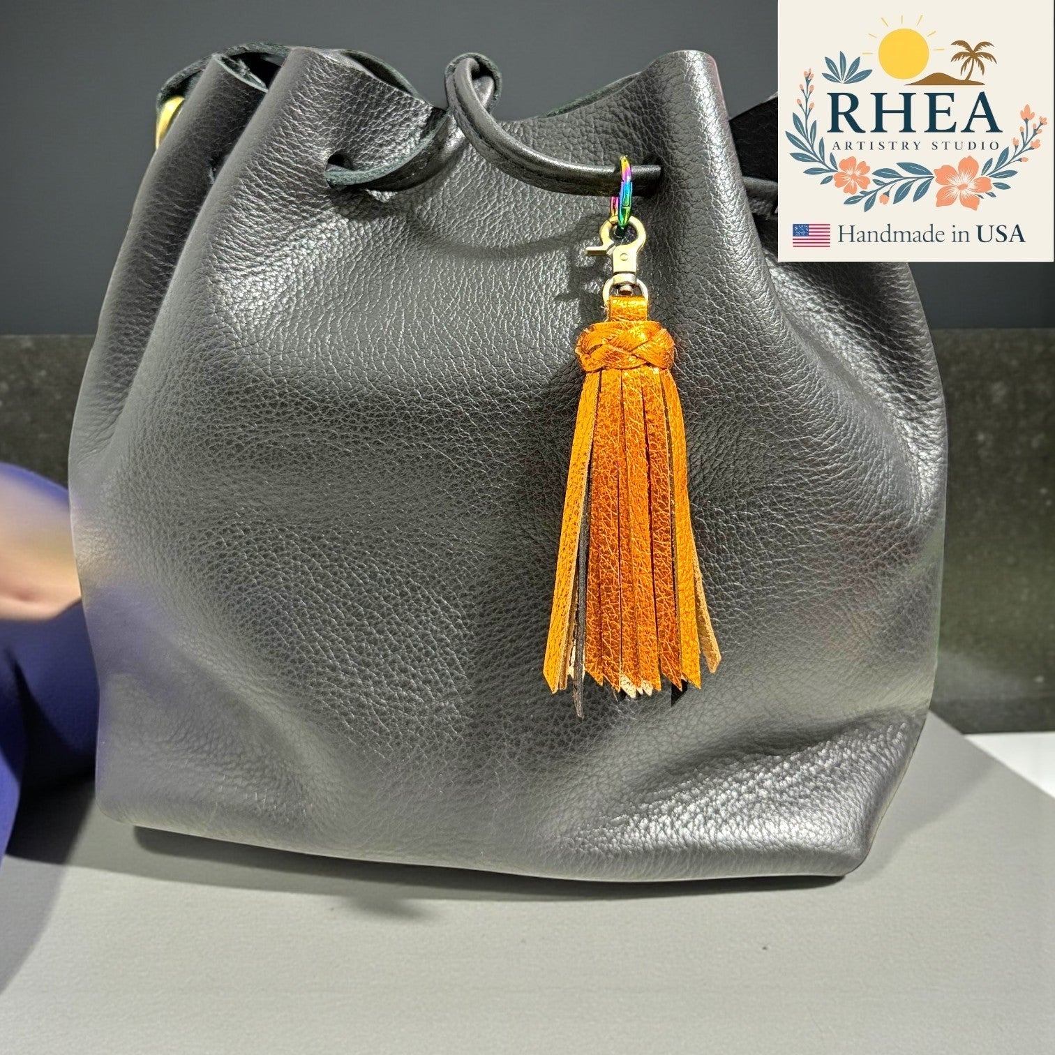 Rhea Artistry Studio handmade orange metallic leather tassel bag charm with antique brass lobster clasp.