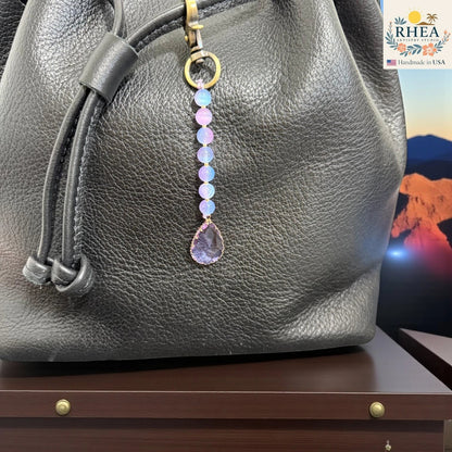 Rhea Artistry Studio handmade pastel beaded bag charm with a faceted purple teardrop pendant and brass clasp.