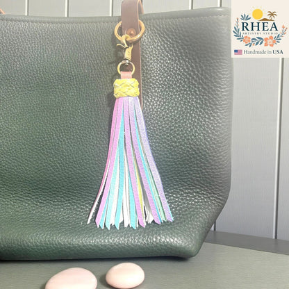 Rhea Artistry Studio pastel leather tassel keychain with lobster clasp attached to a dark green pebbled leather tote bag.