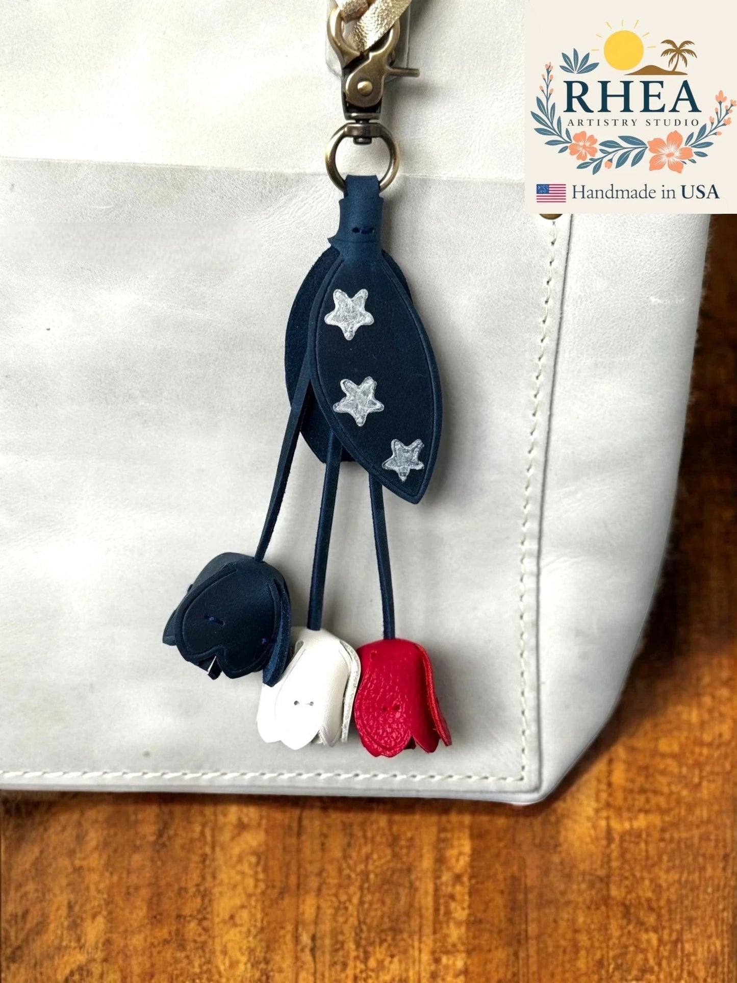 Rhea Artistry Studio patriotic leather charm with navy blue leaves adorned with silver stars and dangling red, white, and blue tulip-shaped charms.