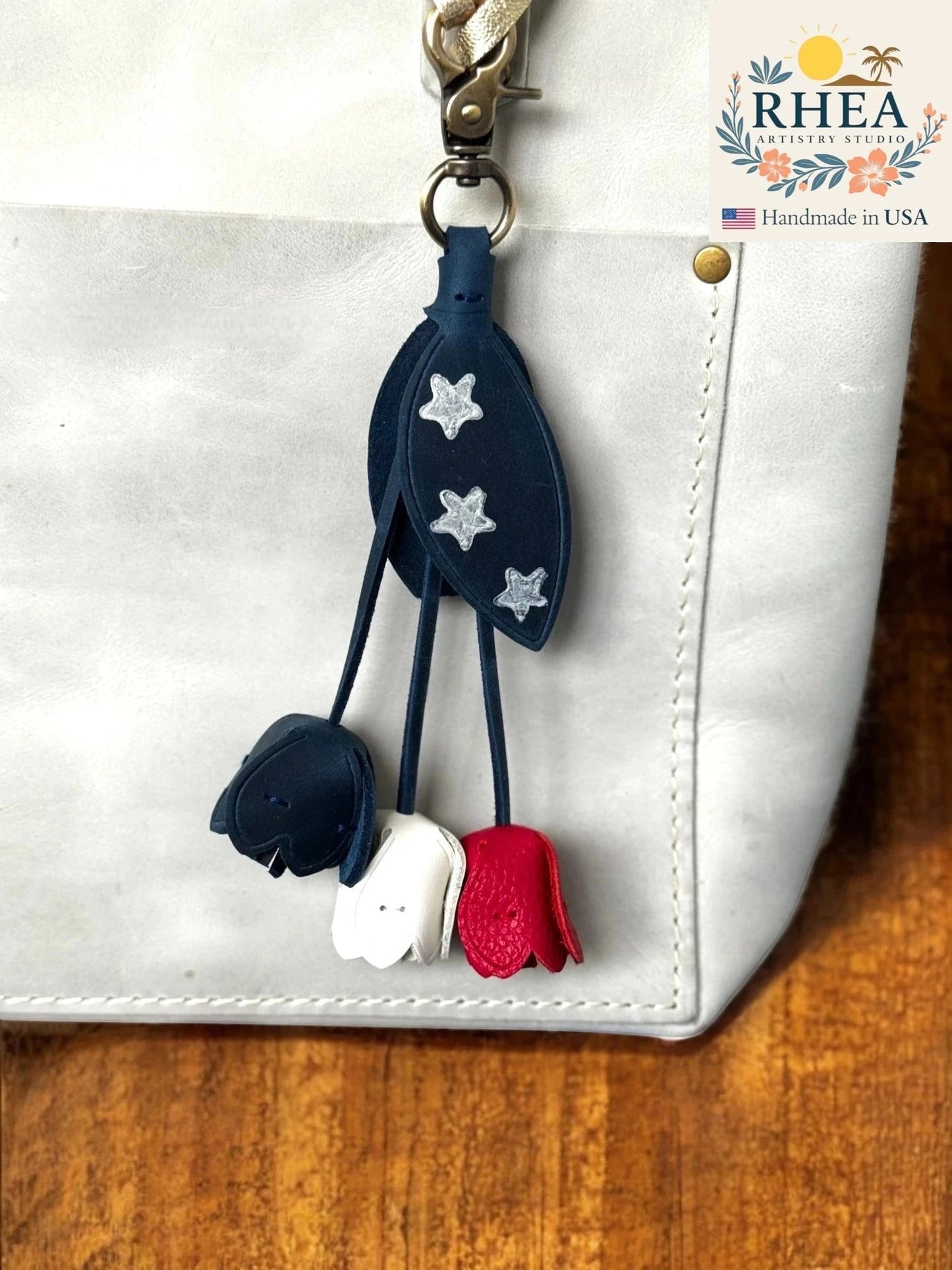 Rhea Artistry Studio patriotic leather charm with navy blue leaves adorned with silver stars and three dangling tulip-shaped charms in navy, white, and red.