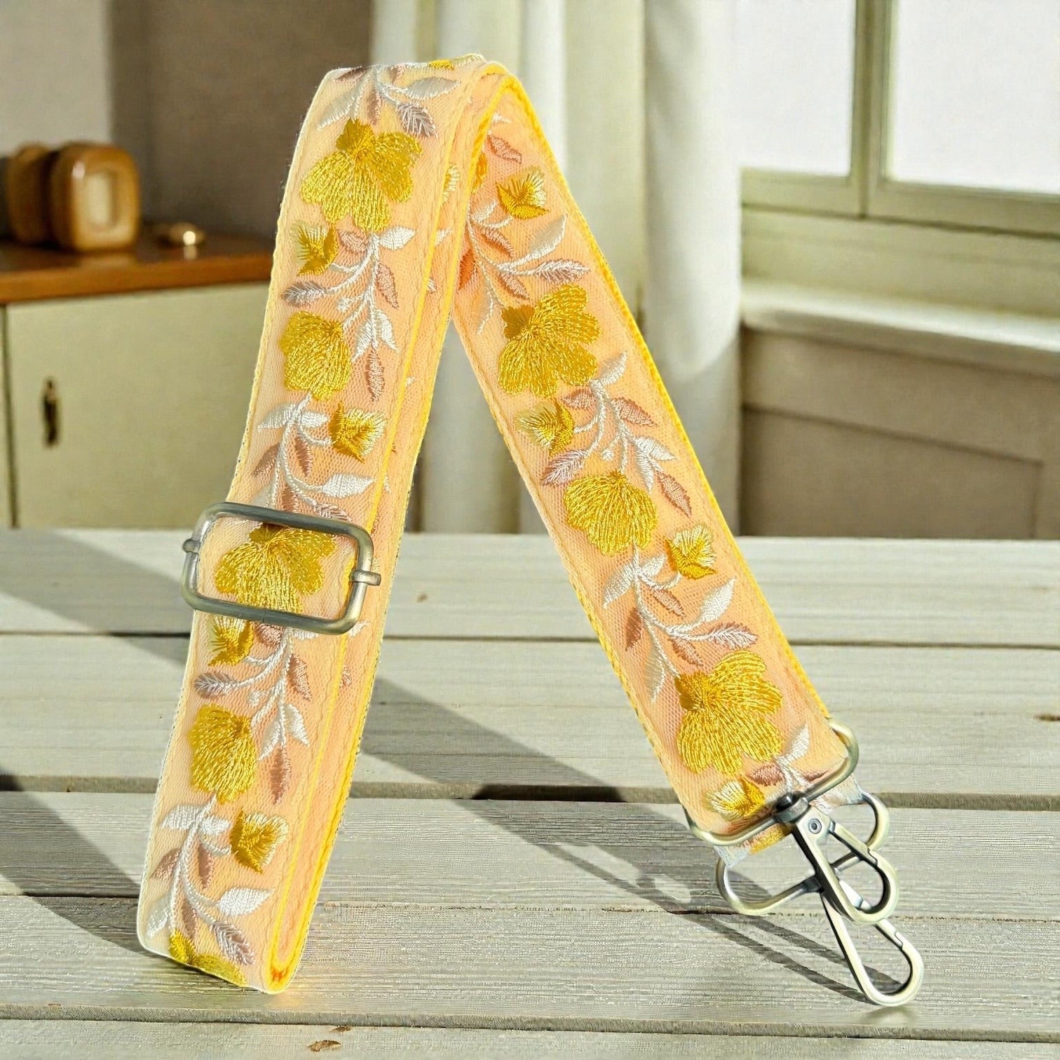 Rhea Artistry Studio peach crossbody strap with yellow floral embroidery and brushed brass hardware.