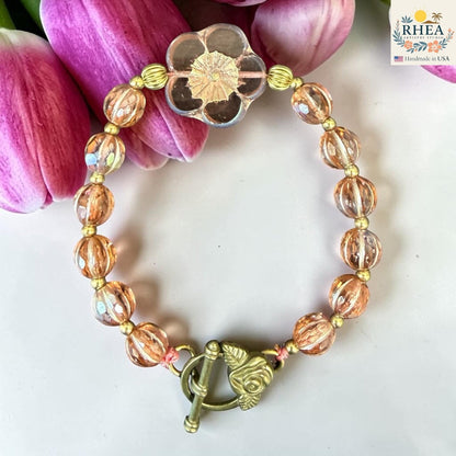 Rhea Artistry Studio handmade peach glass bead bracelet with floral focal bead and brass toggle clasp.