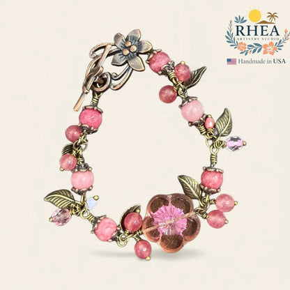 Rhea Artistry Studio handmade blush pink gemstone and glass bead bracelet with floral and leaf motifs and antique brass toggle clasp.
