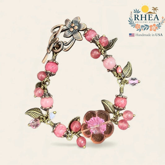 Rhea Artistry Studio handmade blush pink gemstone and glass bead bracelet with floral and leaf motifs and antique brass toggle clasp.