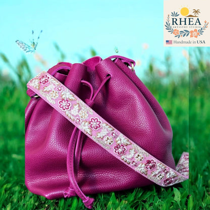 Rhea Artistry Studio pink embroidered lace crossbody strap with floral pattern and brushed brass hardware, shown on a magenta bucket bag.