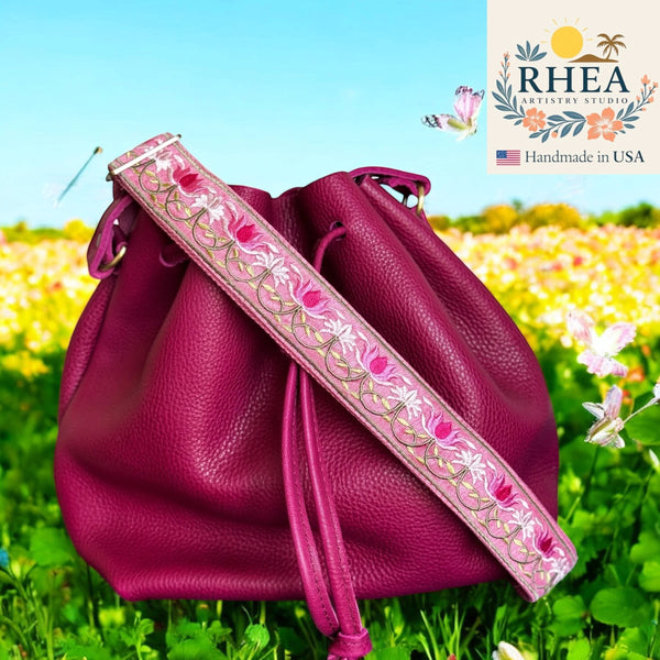 Rhea Artistry Studio pink embroidered lotus bloom crossbody strap with brushed brass hardware on a magenta leather bucket bag.