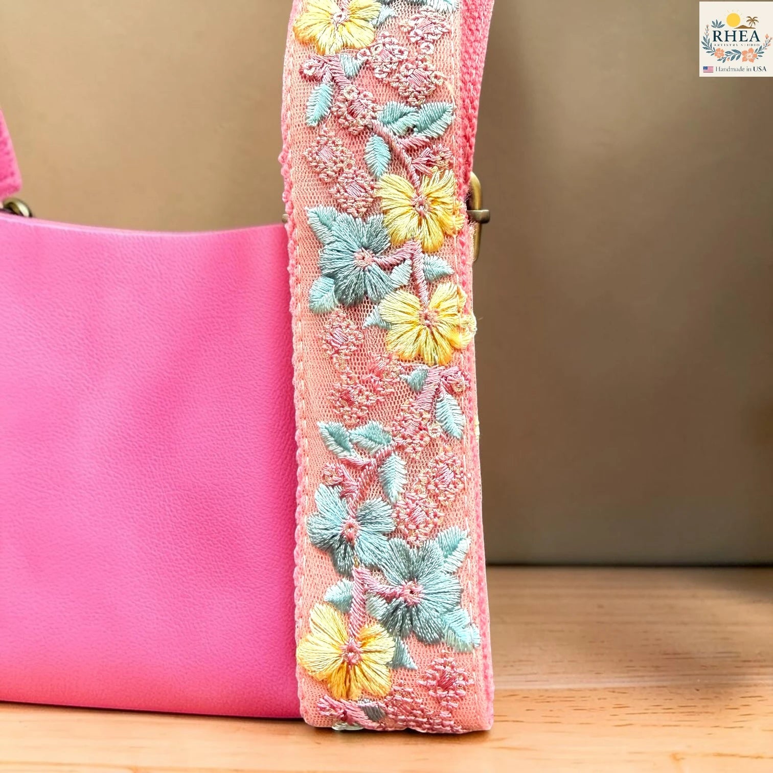 Rhea Artistry Studio blush pink crossbody strap with yellow floral and turquoise leaf embroidery, 1.5-inch width, adjustable length, close-up of embroidery detail.